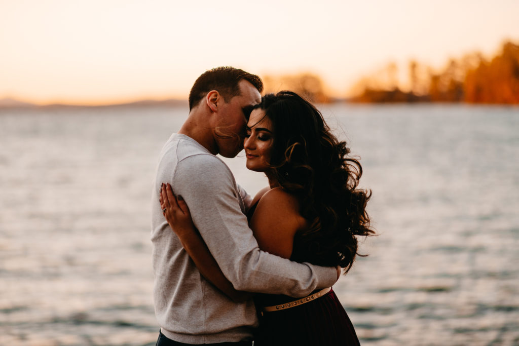 engaged couple holding each other with sunset and water in the background
